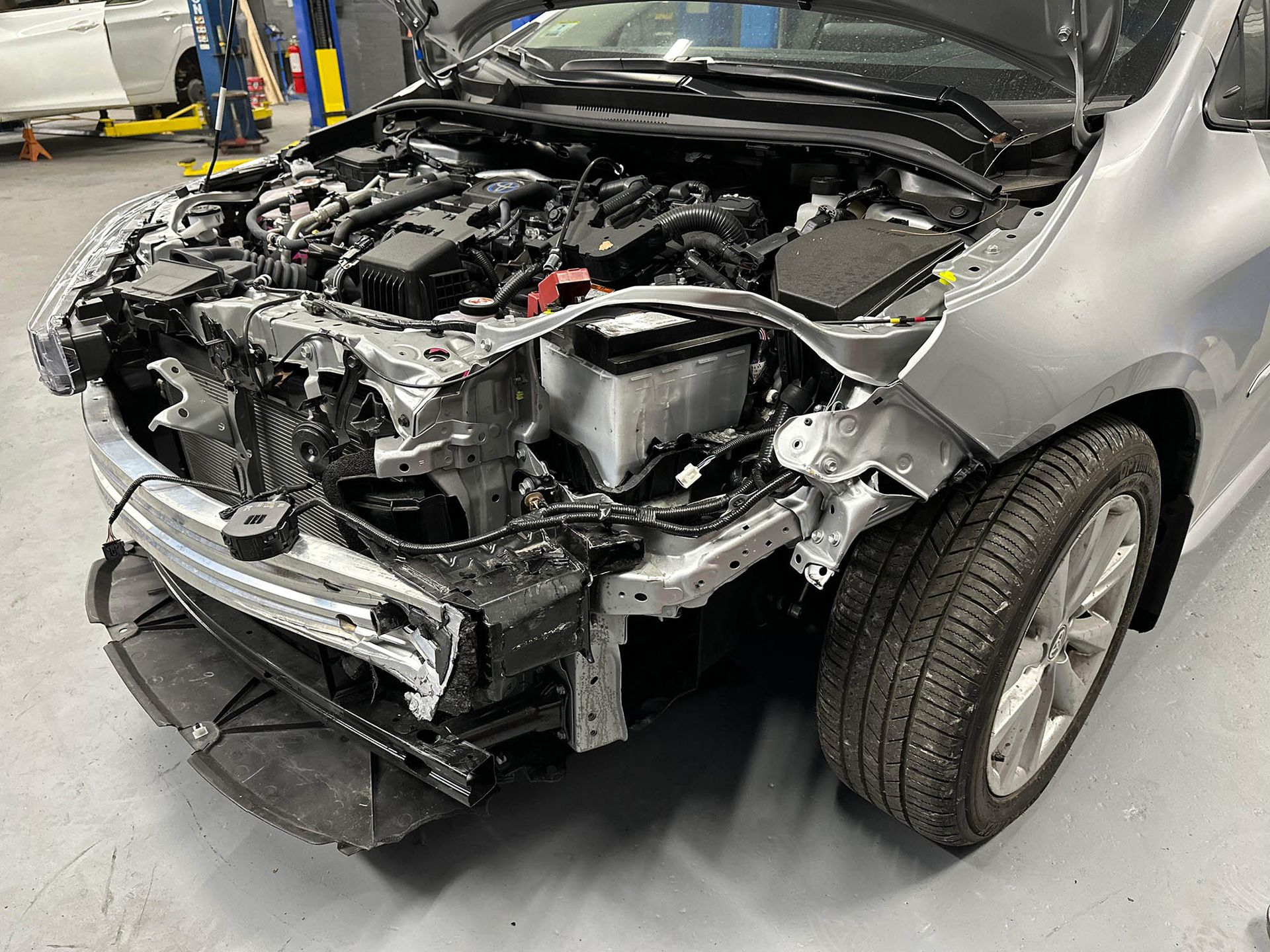 Damaged silver car front end with hood open, showing crushed components. Tire visible.