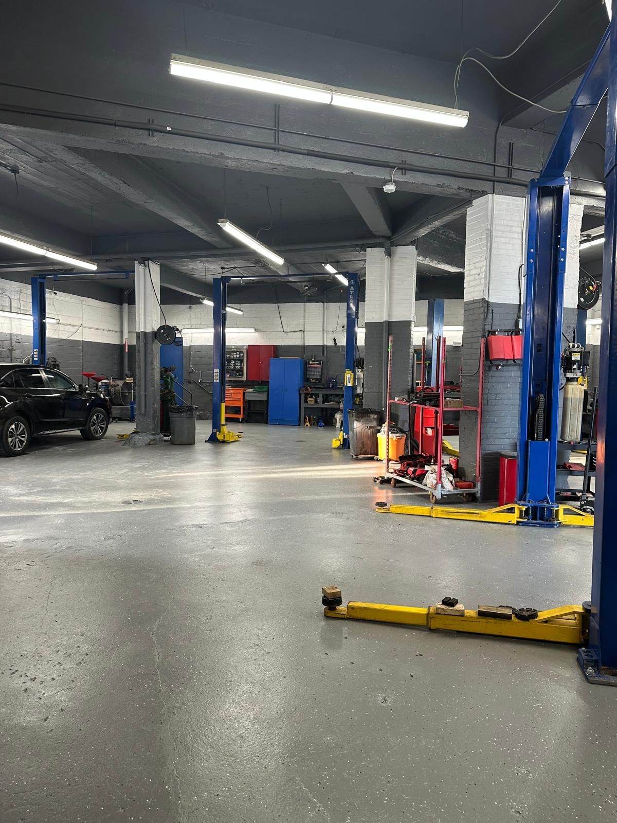 Auto repair shop interior with vehicle lift equipment, tools, and a car. Gray, white, and red accents.