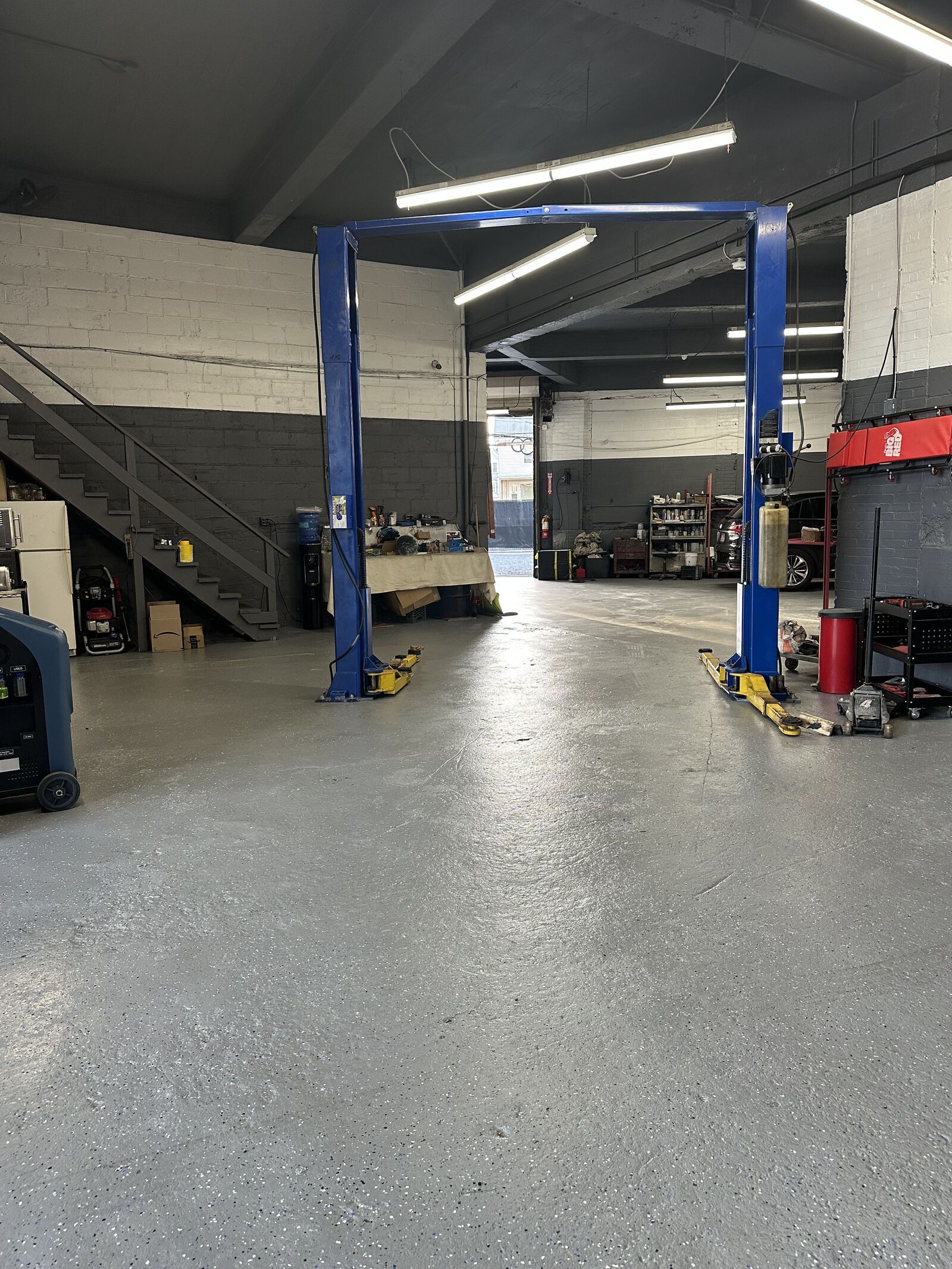 Garage interior with a car lift, gray floor, tools, and stairs.