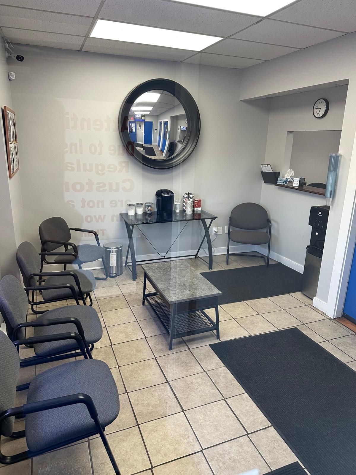 Waiting room with chairs, a coffee station, a mirror, and tiled floor.