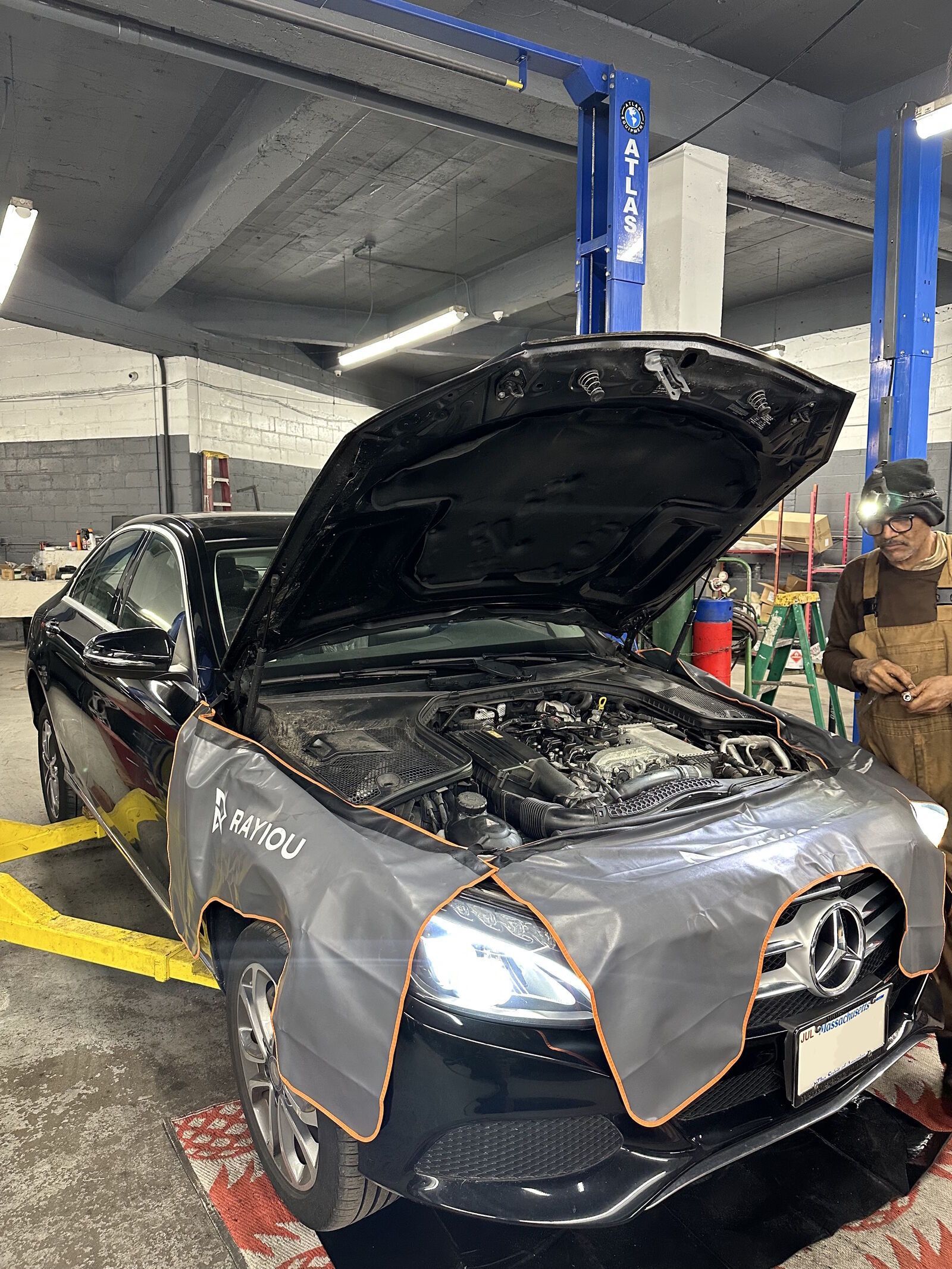 Black car with open hood in a garage, a mechanic stands nearby.