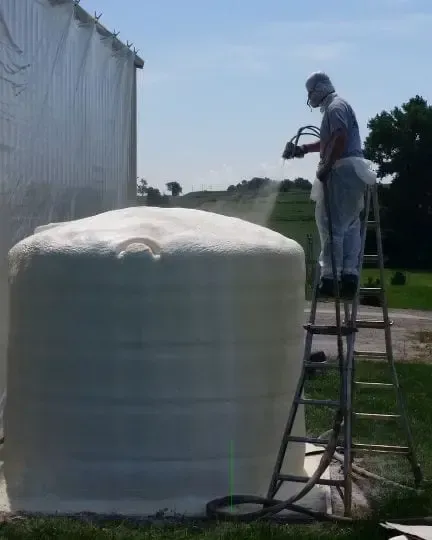 a man standing on a ladder spraying a large white object