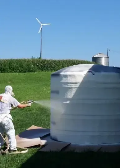 a man is spray painting a large white object in a field with a windmill in the background