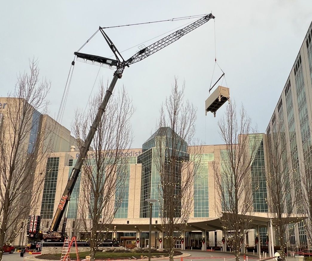 A large crane is lifting a box in front of a building