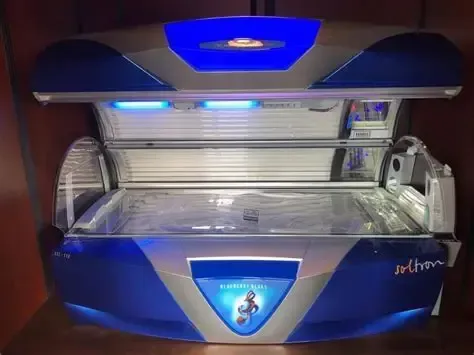 Blue tanning bed with open lid and lit interior, viewed from the front.