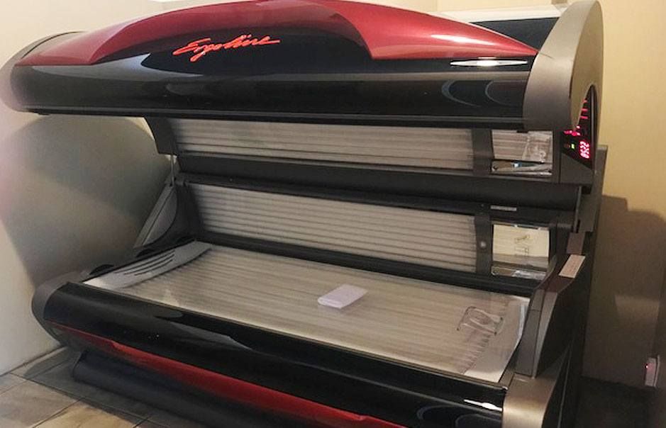 Red and black tanning bed with raised canopy in a salon room