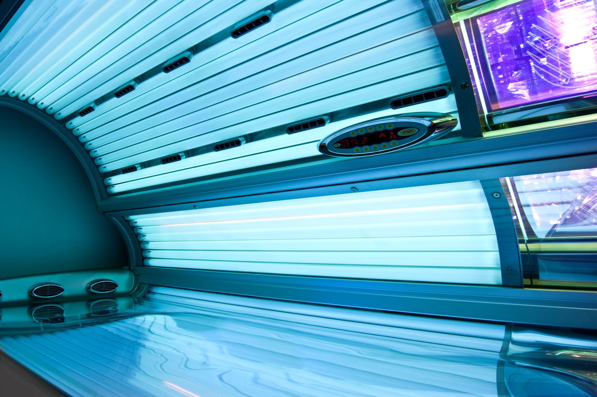 Blue-lit tanning beds lined up in a modern indoor tanning salon