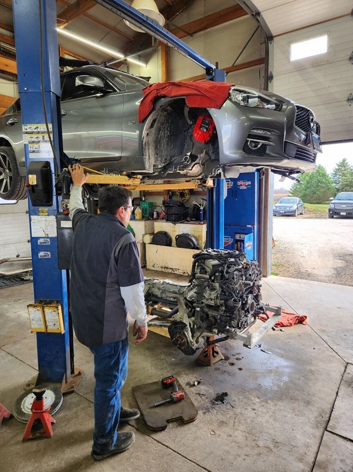Car on a lift in a garage, mechanic working on it, engine on the ground.