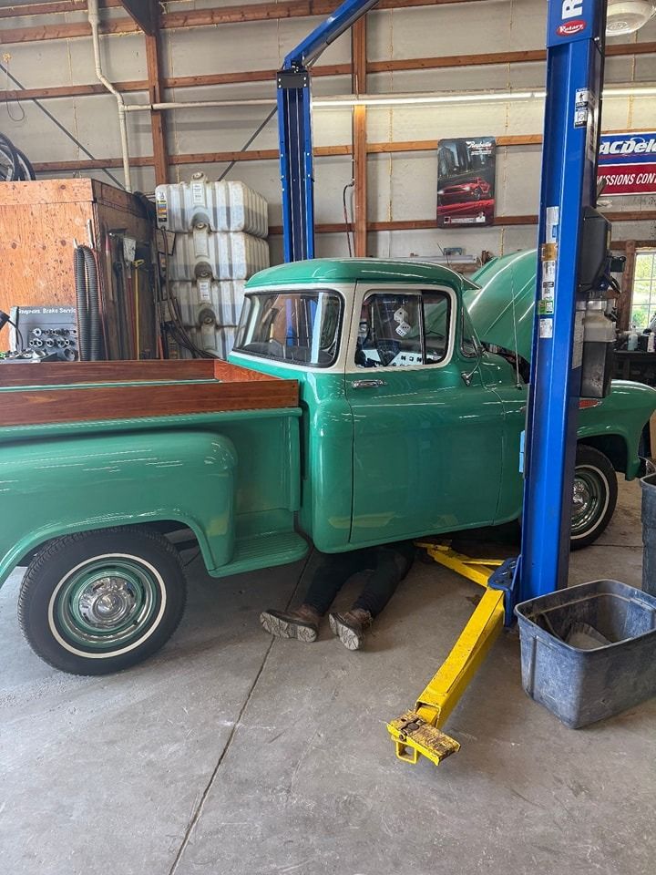 Green vintage truck on a lift in a garage, a person is working underneath it.