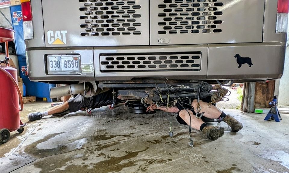 Mechanic working under a large piece of machinery, likely a CAT, in a garage.