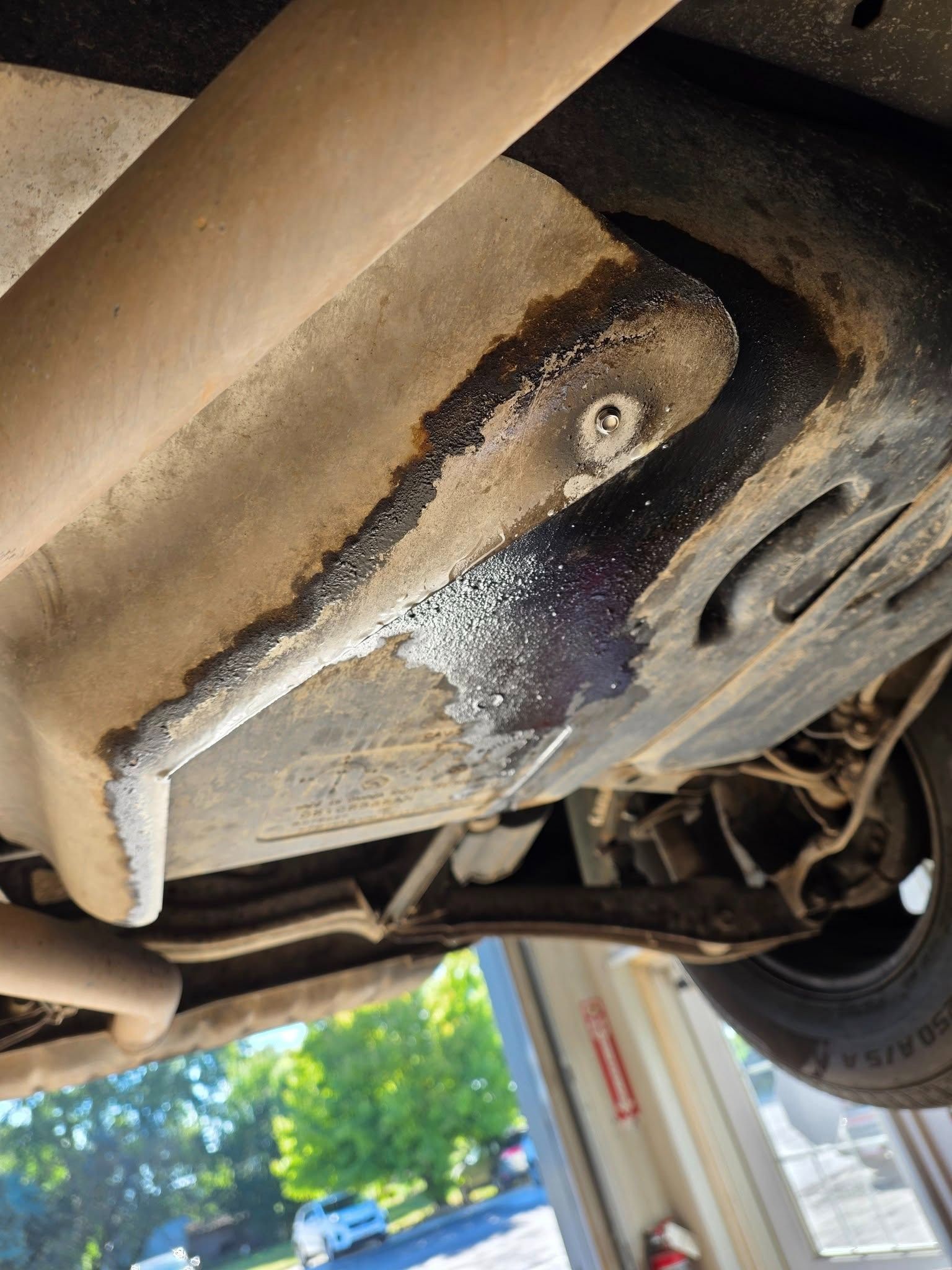 Undercarriage of a vehicle with a metal shield showing fluid stains and a rusty appearance.