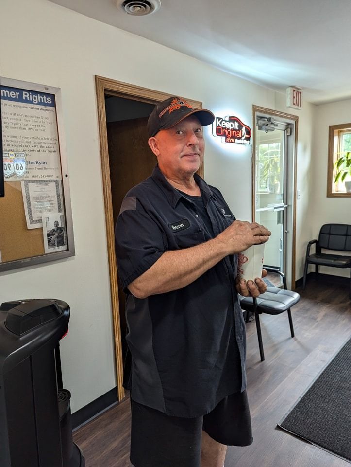 Man in black uniform and cap holds something white, standing near a door and a bulletin board.