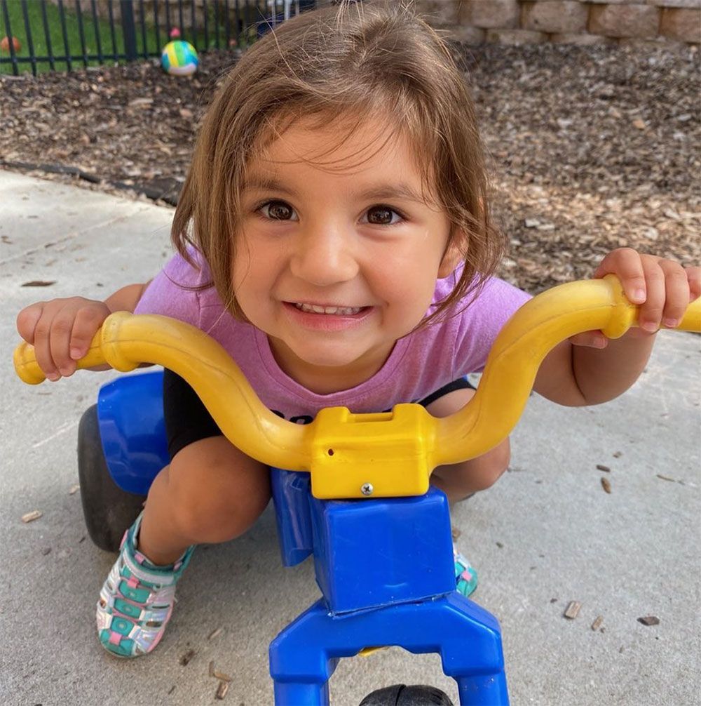 A little girl is riding a blue and yellow bike