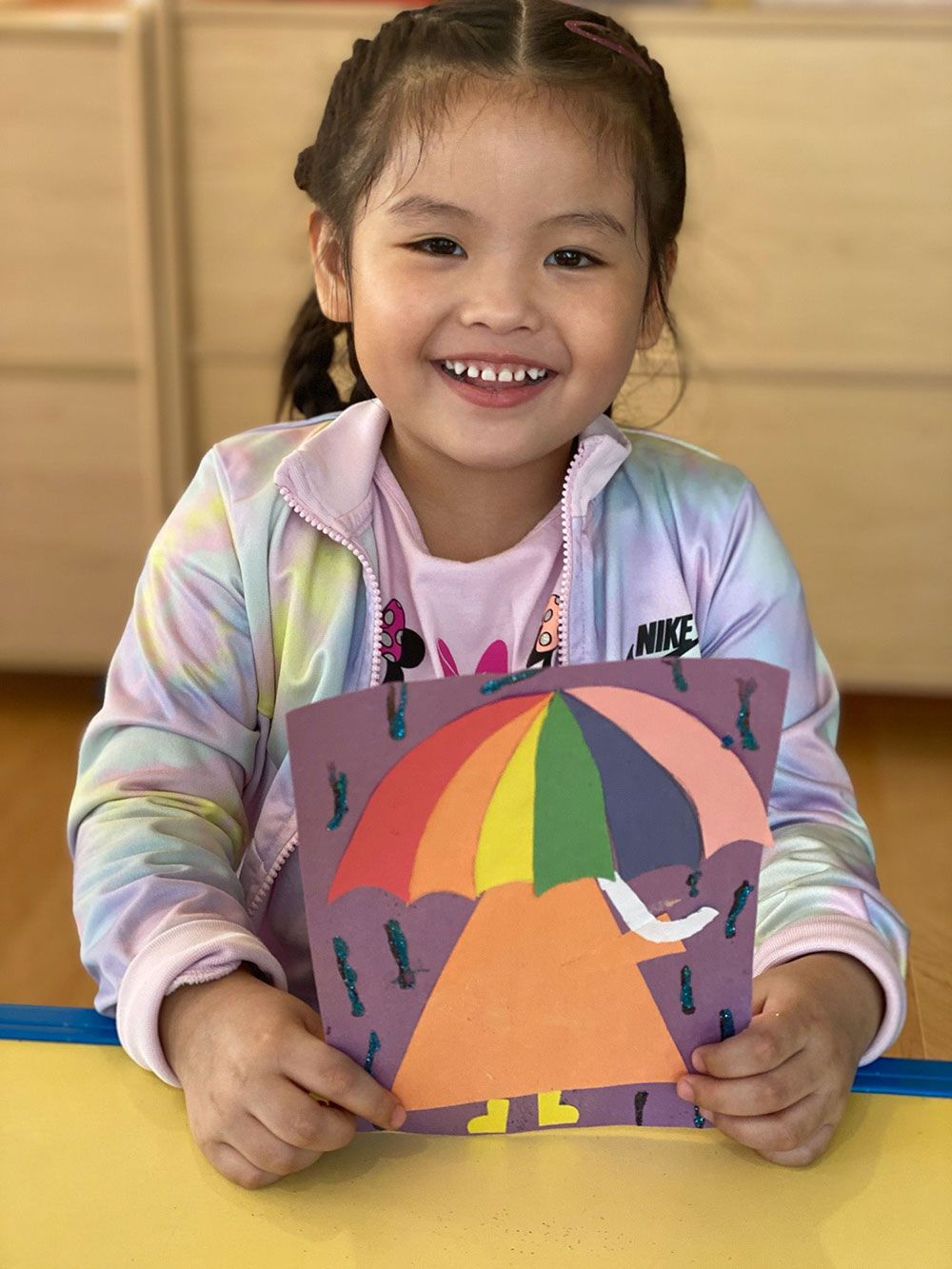 A little girl is holding a piece of paper with an umbrella on it