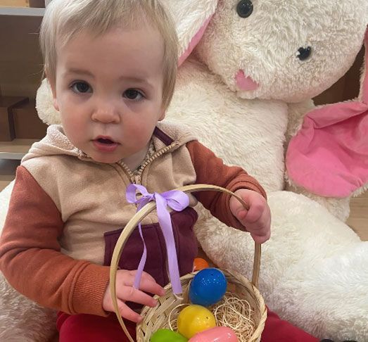A baby is holding a basket of easter eggs