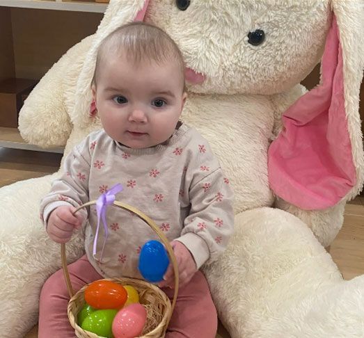 A baby is sitting next to a stuffed bunny holding a basket of easter eggs