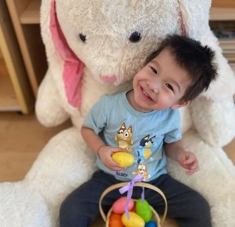 A little boy is sitting next to a stuffed bunny holding a basket of easter eggs