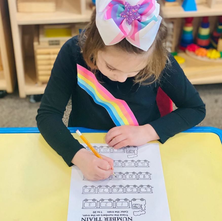 A little girl with a bow on her head is writing on a piece of paper 
