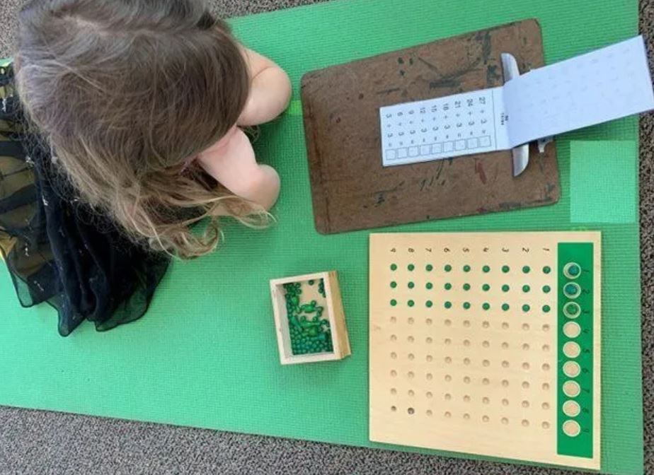 A little girl is sitting on a green mat playing with toys