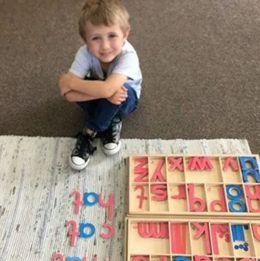 A young boy sits on the floor next to a tray of alphabet letters
