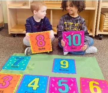 Two children are sitting on the floor holding cards with numbers
