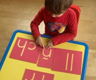 A young boy is sitting at a table playing with sandpaper letters