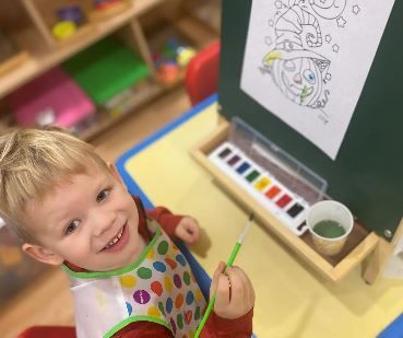 A little boy is sitting at a table painting with watercolors