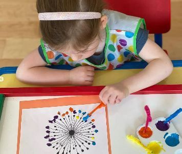 A little girl is sitting at a table painting a fireworks display