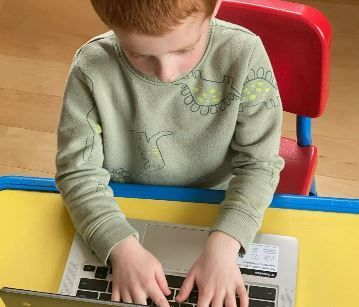 A young boy is typing on a laptop 