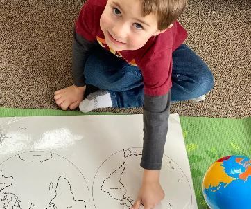 A young boy is sitting on the floor drawing a map of the world