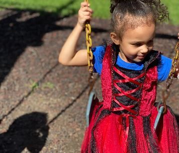 A little girl in a red dress is sitting on a swing