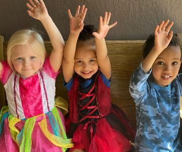 Three children are sitting on a bench with their hands in the air