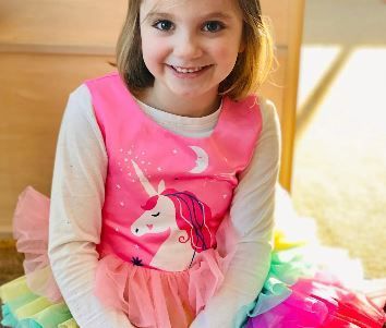 A little girl in a pink unicorn dress is sitting on the floor