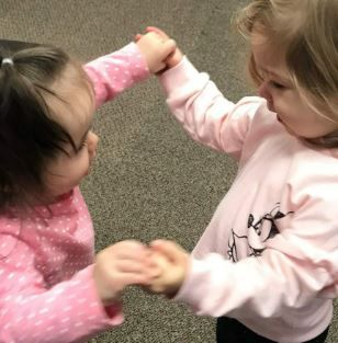 Two little girls are holding hands and playing with each other.