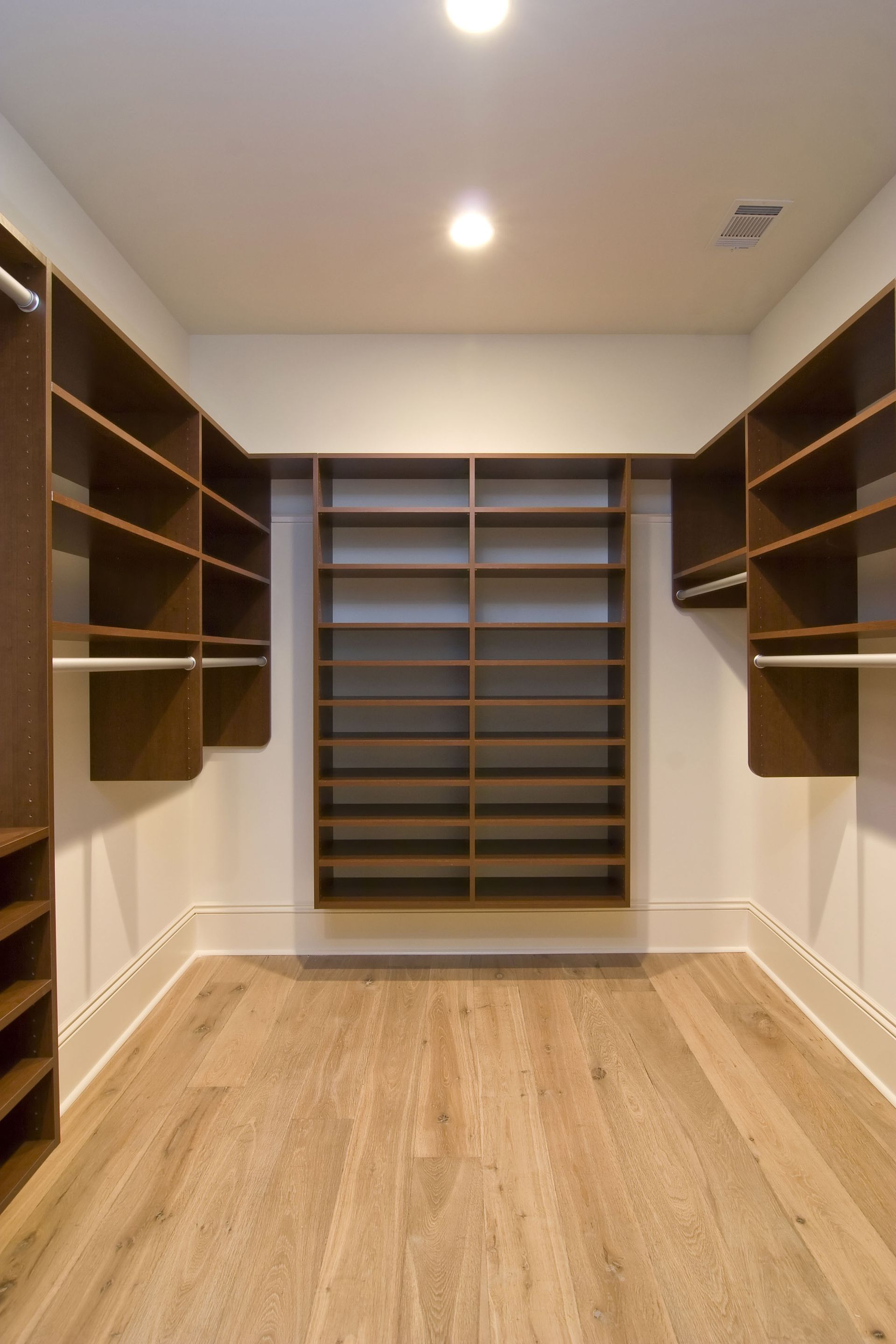 Walk-in closet with wooden shelves and hanging rails on both sides, empty wood floor, and recessed ceiling lights