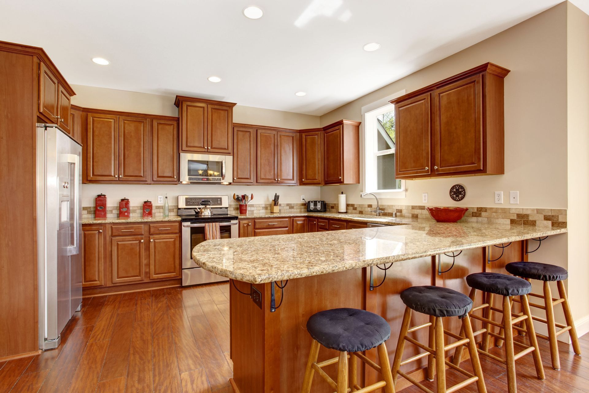 Bright kitchen with wooden cabinets, granite island, stainless appliances, and four bar stools