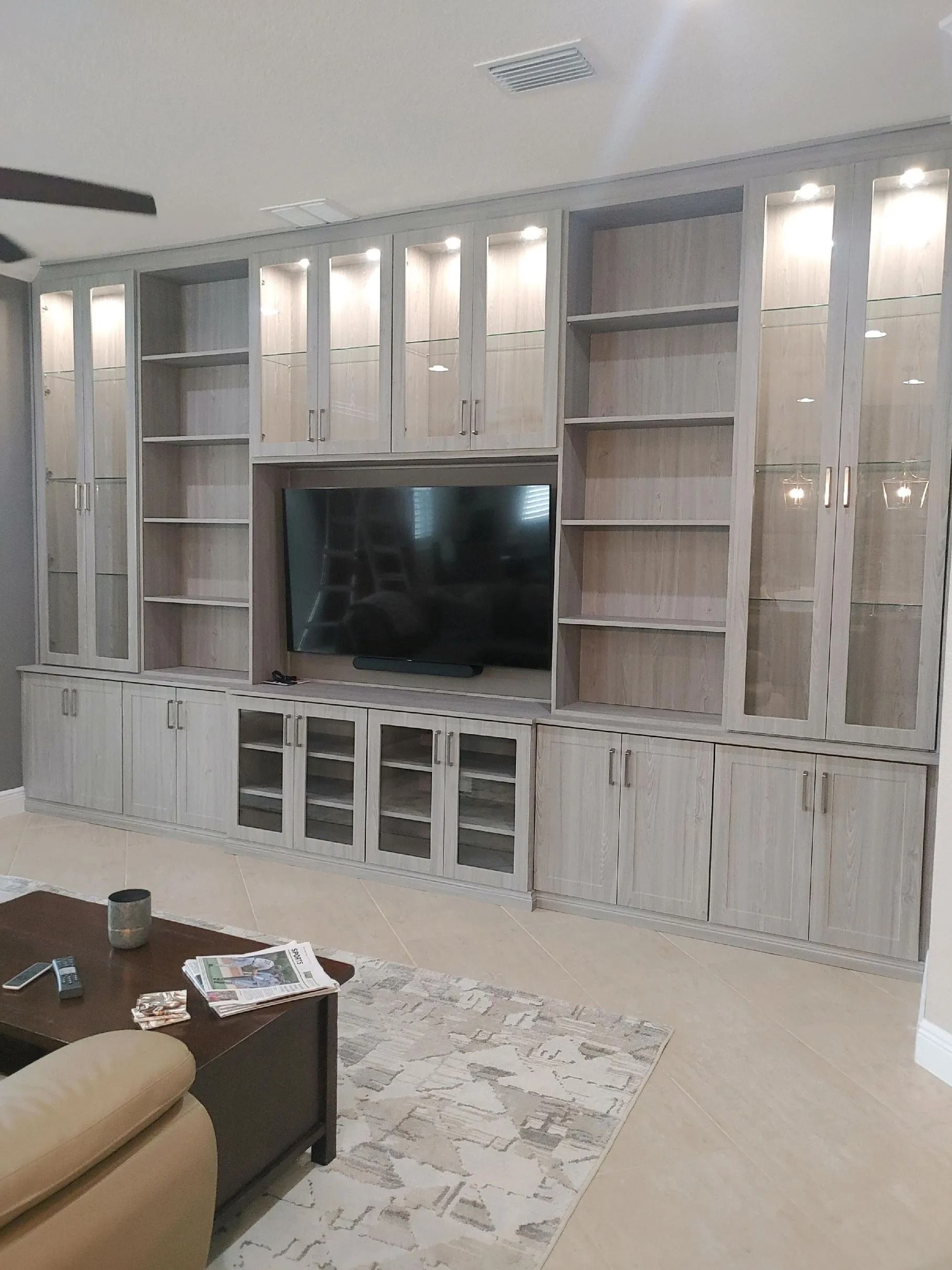 White built-in living room wall units with a large TV and glass cabinet doors.
