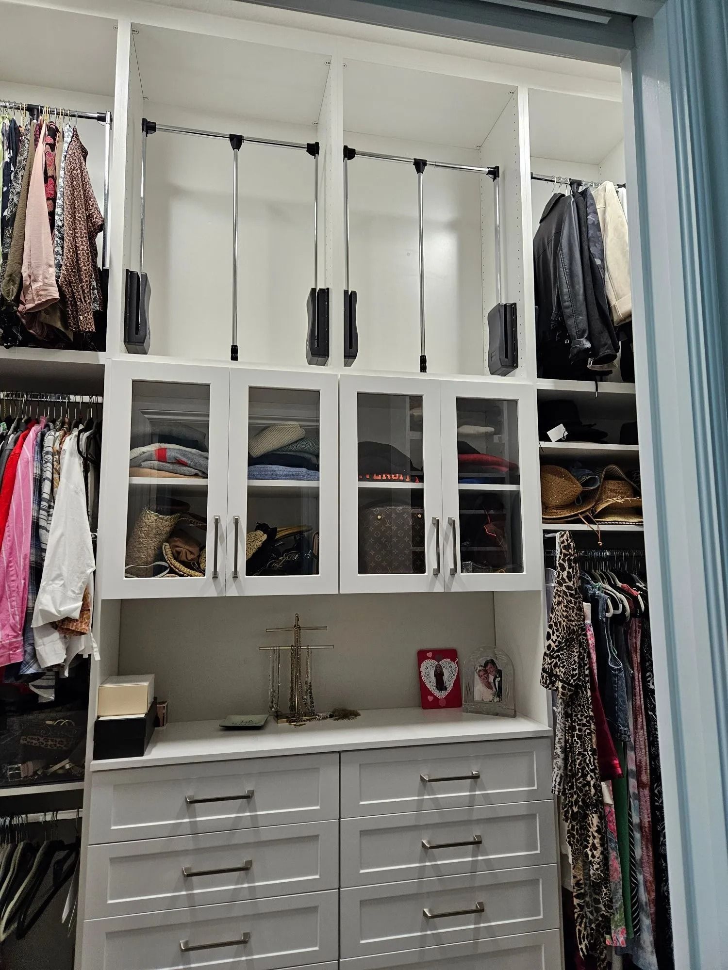 White closet with built-in drawers, shelves, hanging clothes, and mirrored cabinet doors.