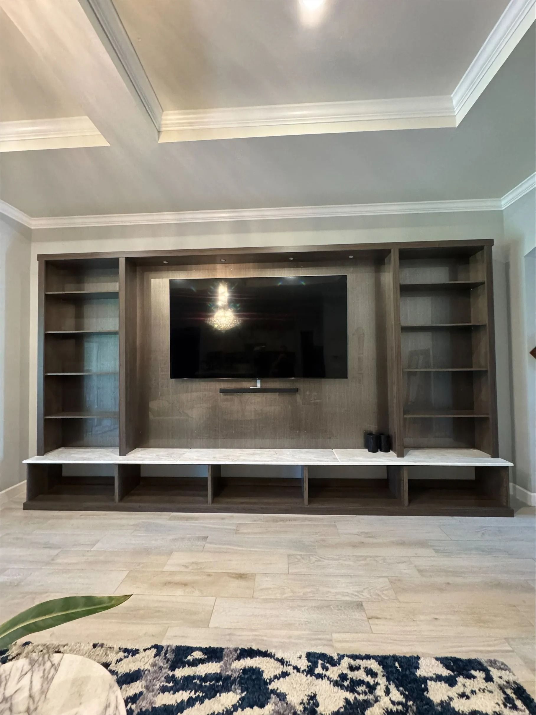 Living room wall with built-in gray shelving, a mounted TV, and a long bench below.