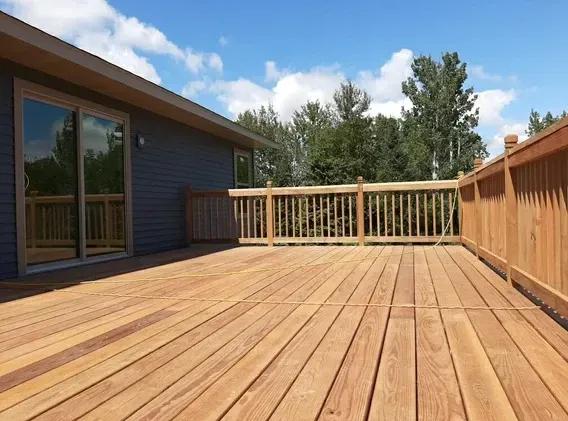 An empty wooden deck with a fence and sliding glass doors.