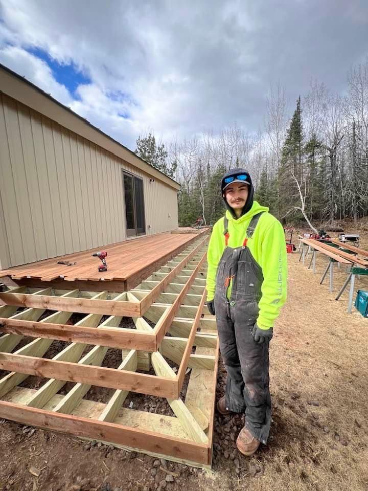 A small house with a deck in the backyard surrounded by trees.