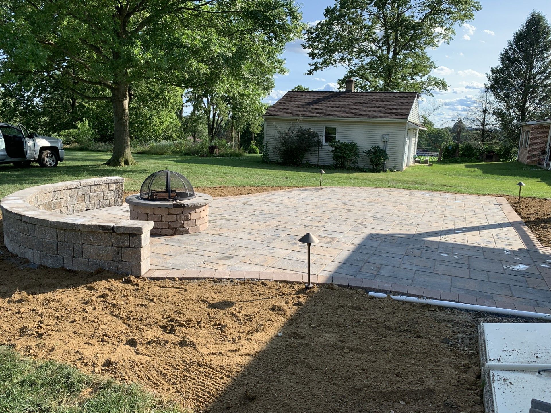 Backyard patio with brick fire pit, curved stone bench, and small white shed under trees