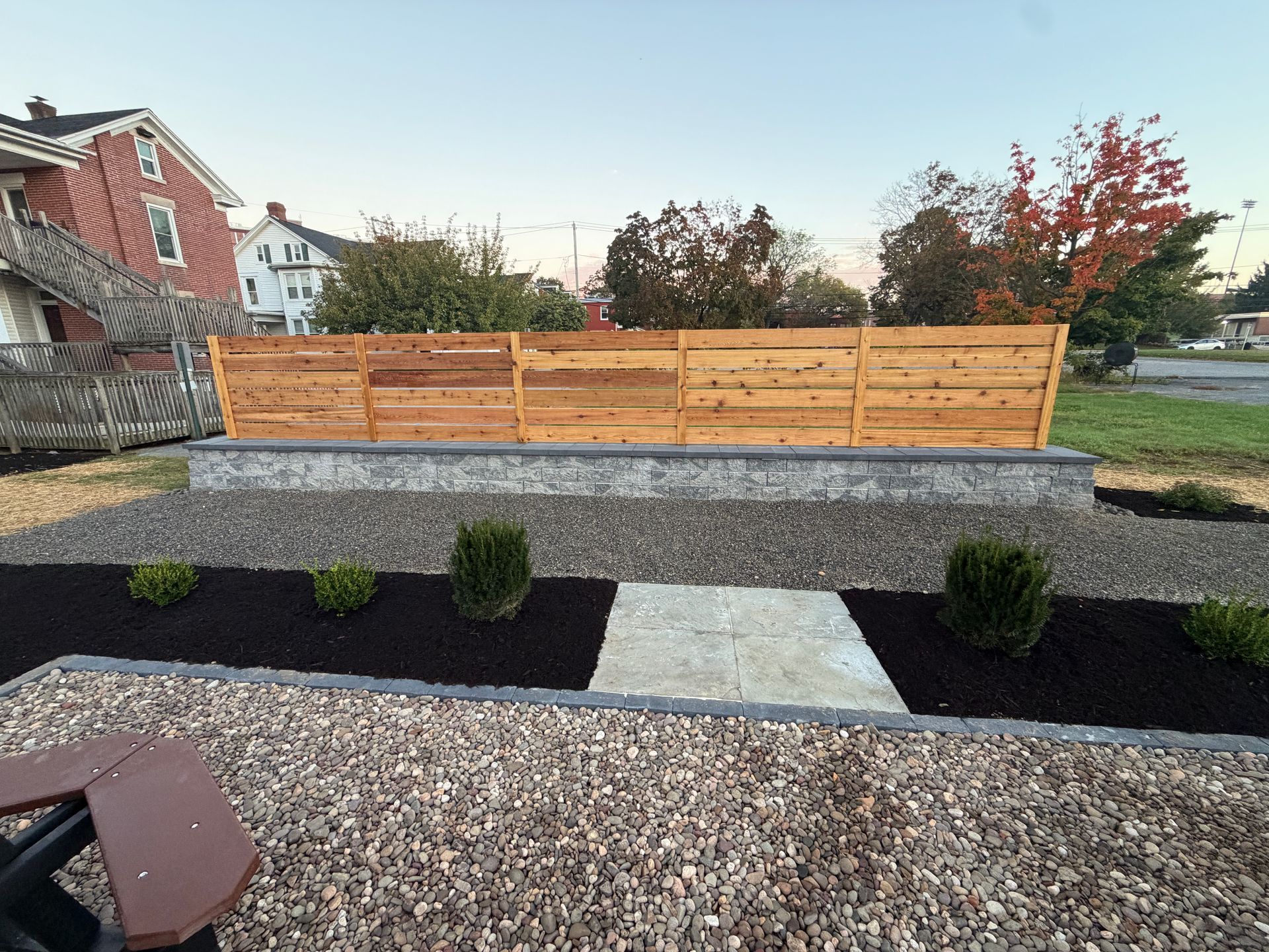 Modern backyard landscaping with gravel paths, black mulch beds, small shrubs, and a wooden fence.