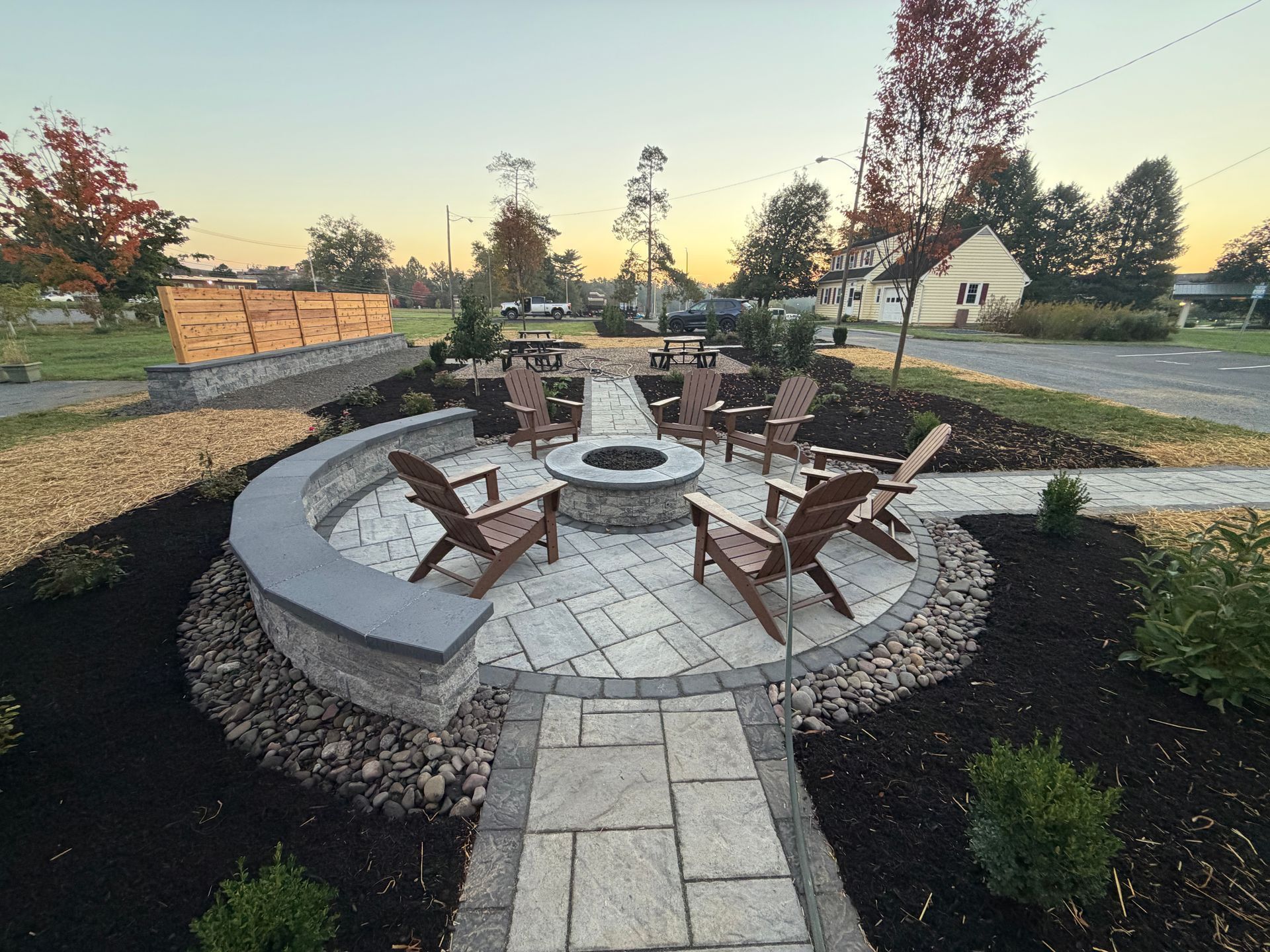 Circular stone fire pit with Adirondack chairs in a landscaped backyard at sunset