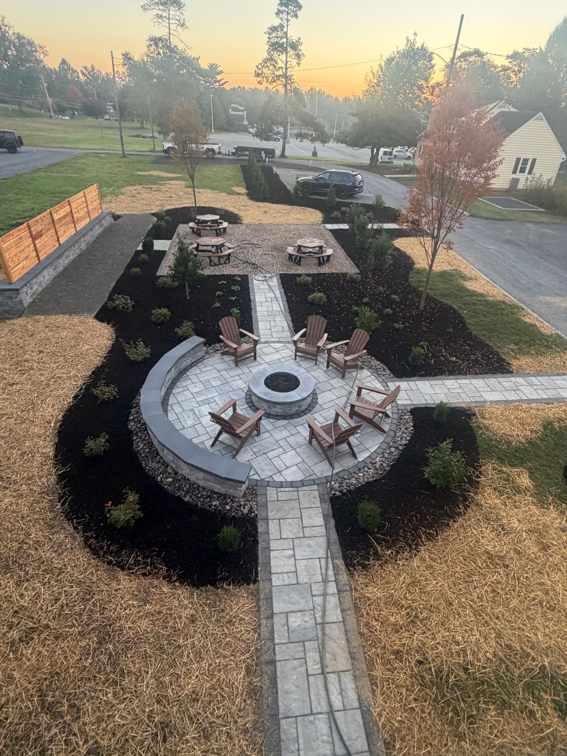 Backyard patio with circular stone fire pit, built-in seating, and manicured landscaping at sunset