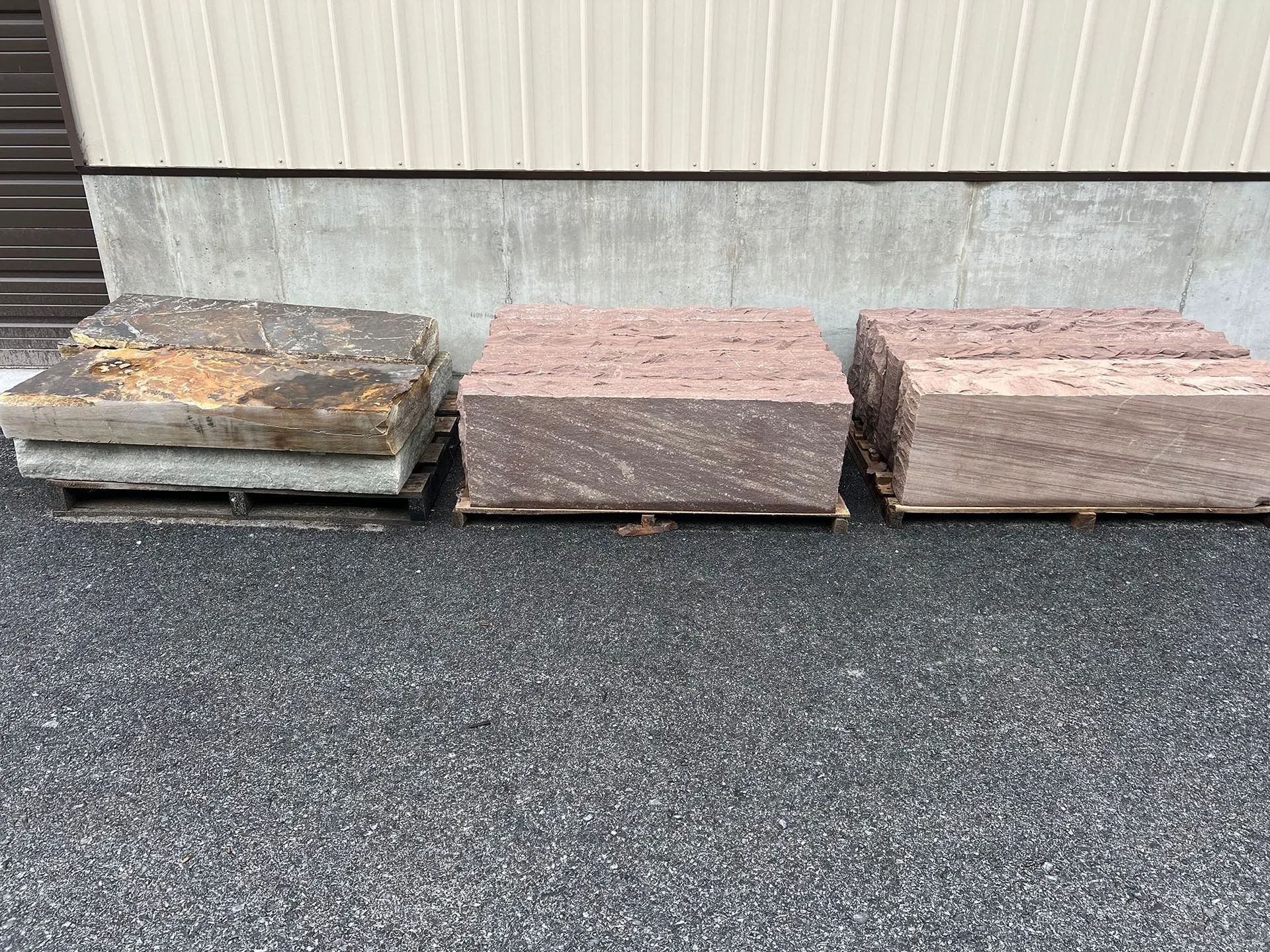 Three stacked stone slabs on a paved surface beside a corrugated metal wall