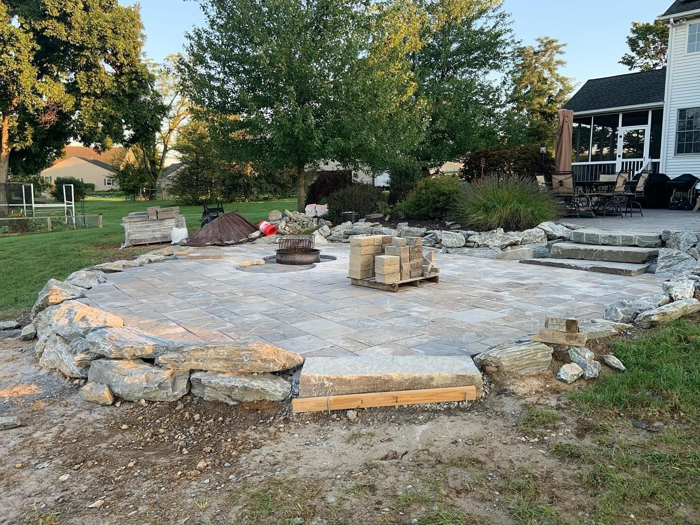 Stone patio with a fire pit and low rock seating in a backyard yard.