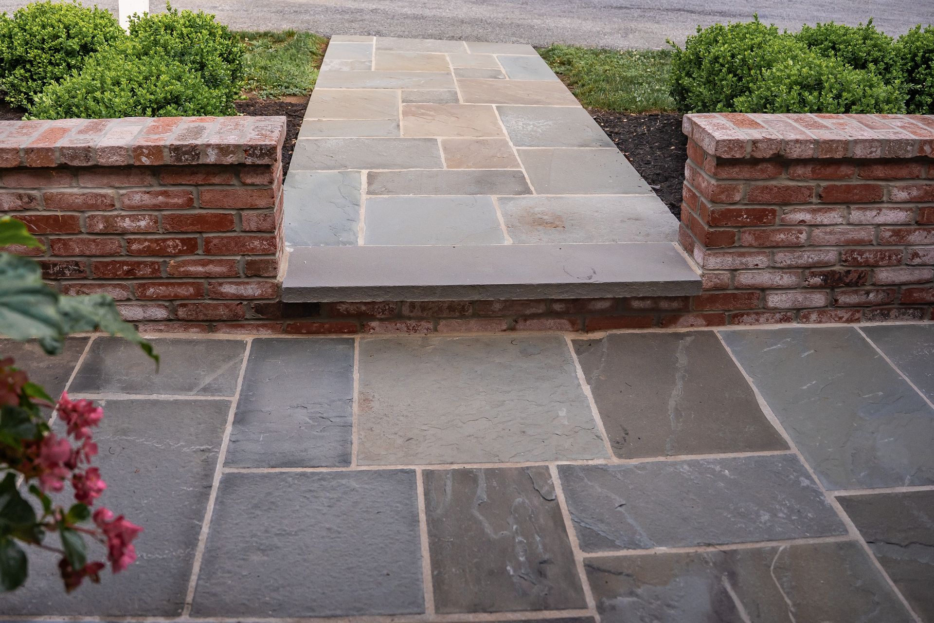Stone walkway with low brick steps leading to a landscaped garden path and shrubs