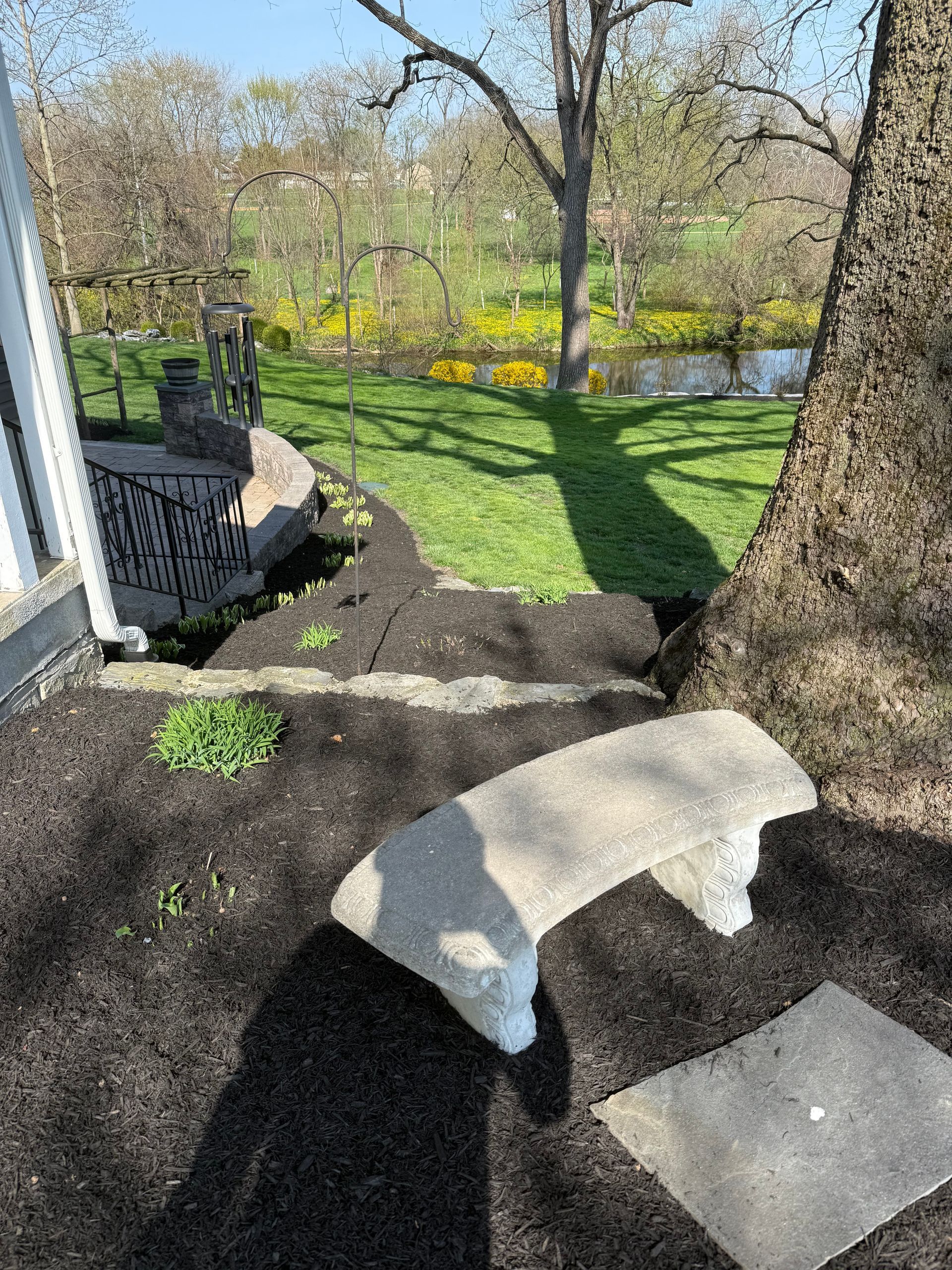 Backyard with stone stepping pads, mulch, grass, trees, and spring flowers near a house.