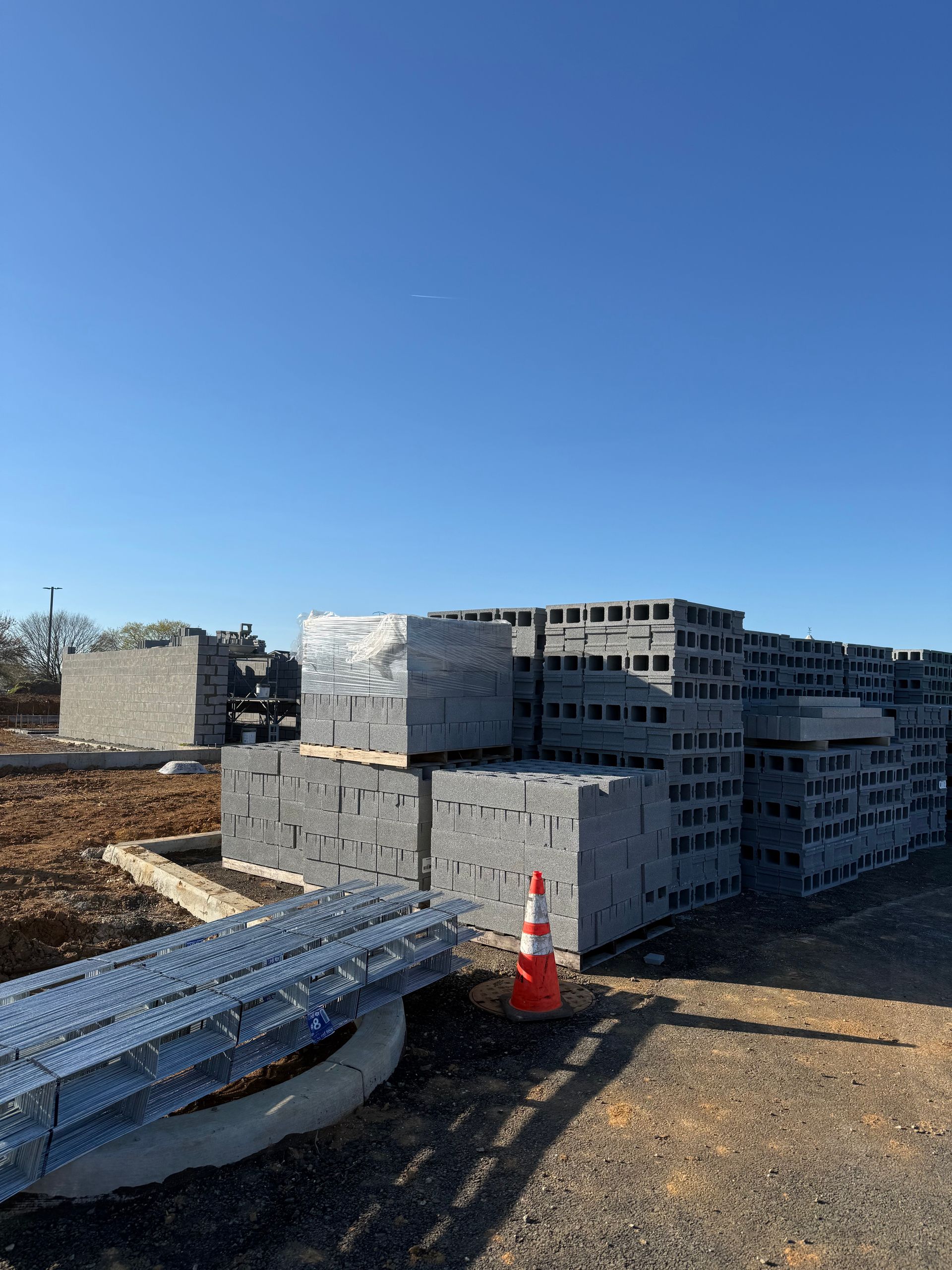 Stacks of gray cinder blocks and pallets at a construction site under a clear blue sky